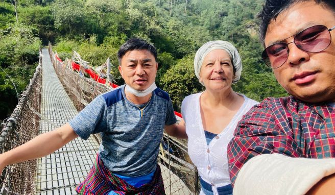 Fran Bak steht auf einer Hängebrücke mit ihrem Guide Gembo NB (l) und ihrem Fahrer Tashi Tshering. Sie ist seit der Pandemie die erste Touristin, die Urlaub im Königreich Bhutan machen darf.