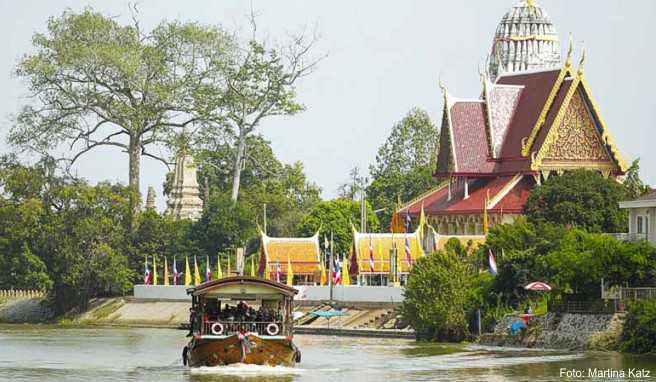 Gemütlich tuckert eine ehemalige Reisbarke auf dem Chao Phraya an der Tempelanlage Wat Phuttaisawan südlich der Altstadt von Ayutthaya vorbei