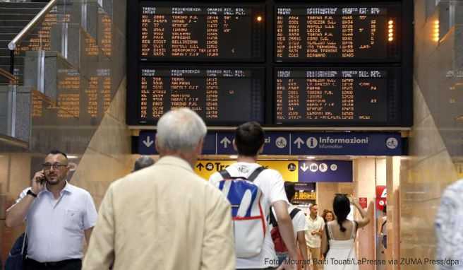 Reisende gehen unter einer Fahrplananzeige am Mailänder Hauptbahnhof
